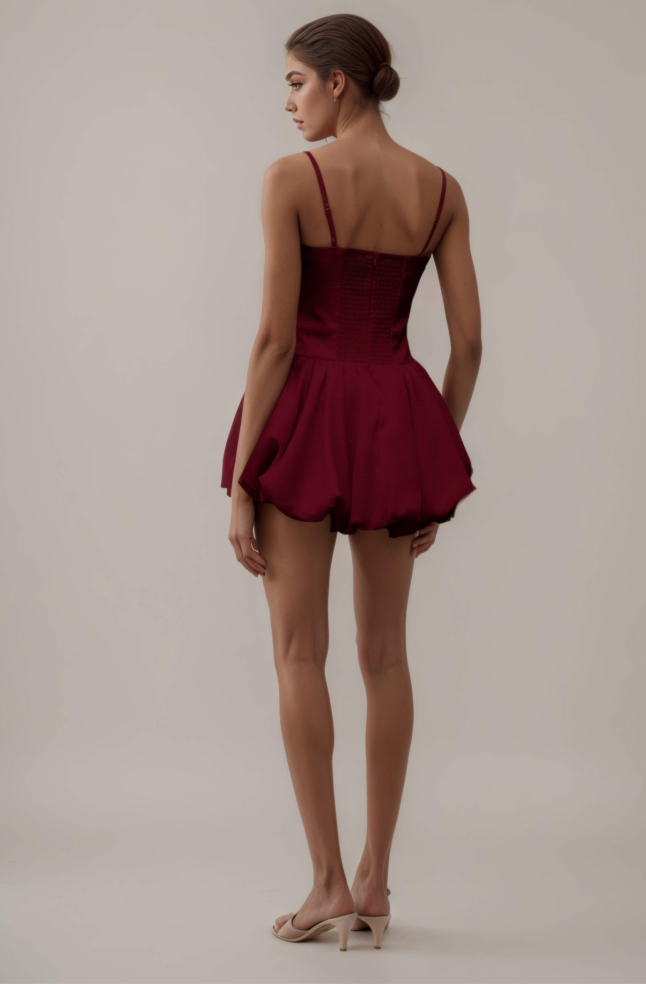 Woman wearing a burgundy dress with thin straps on a plain background